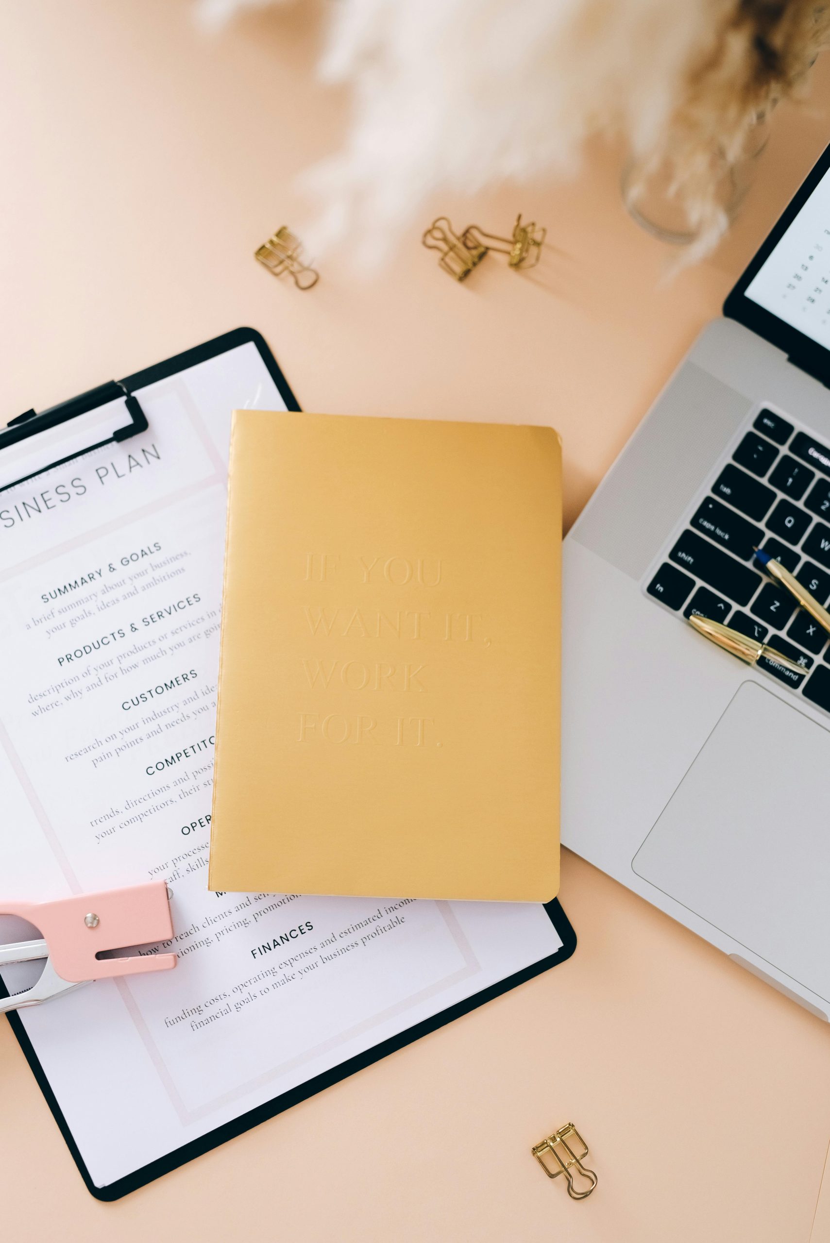 Yellow notebook with a motivational quote placed in front of a clipboard displaying a business plan checklist — symbolising planning, productivity, and positive mindset.